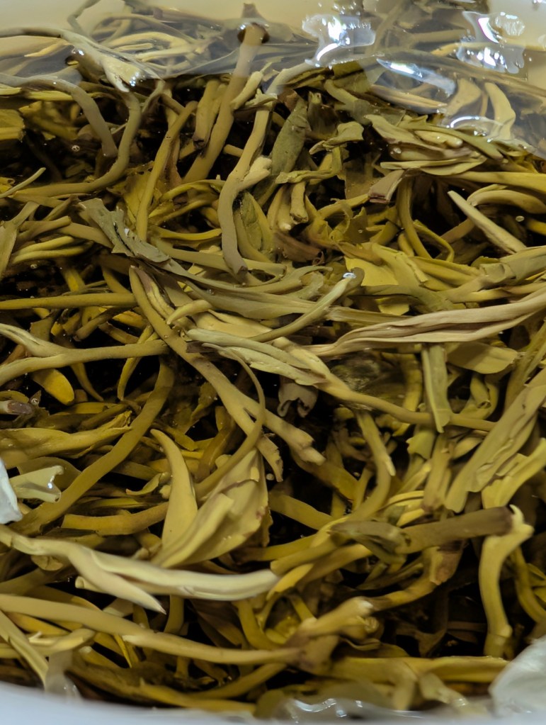 Close-up view of loose, dried jasmine tea leaves in a bowl, showcasing their delicate shapes and hues.