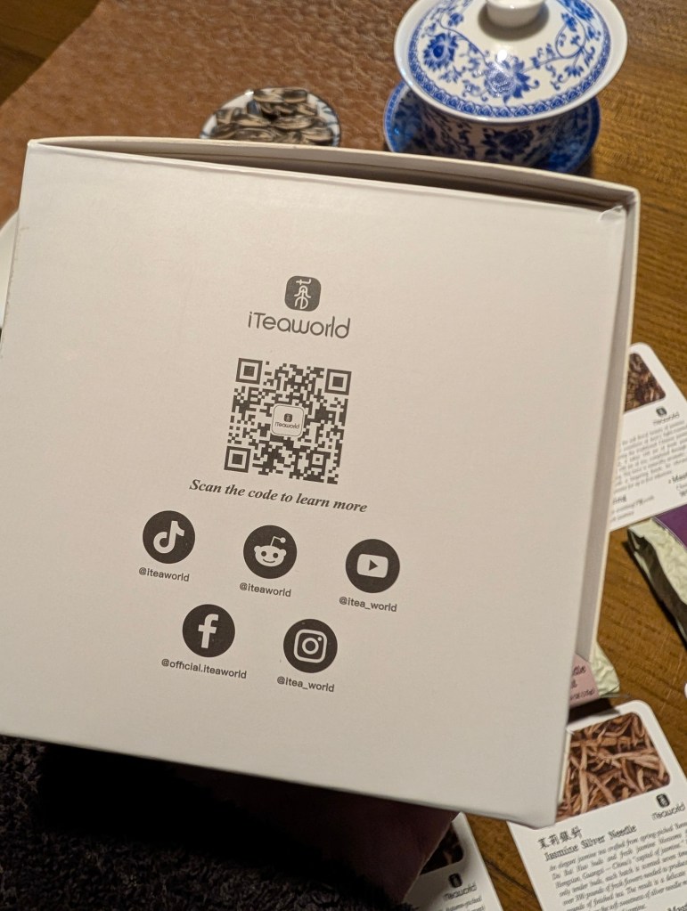 A close-up image of the iTeaworld Jasmine Tea Discovery box featuring a QR code for more information, alongside educational tea cards and a traditional tea set in the background.