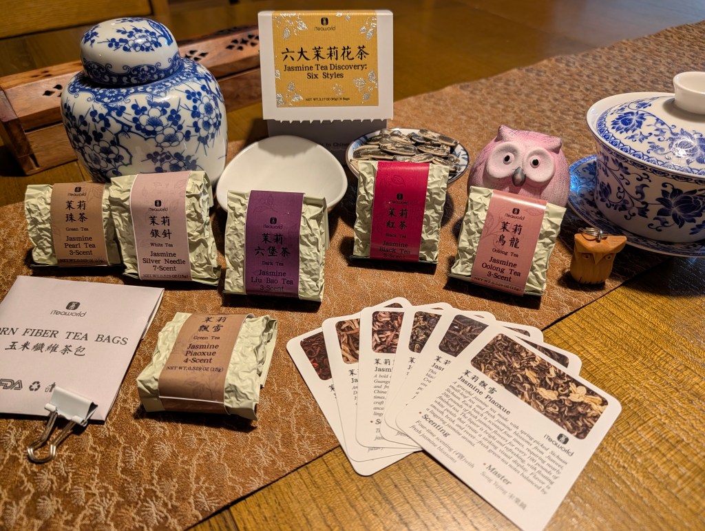 A well-arranged Jasmine Tea Discovery box from iTeaworld featuring various jasmine teas, educational cards, and a decorative tea pot, all set on a wooden table.